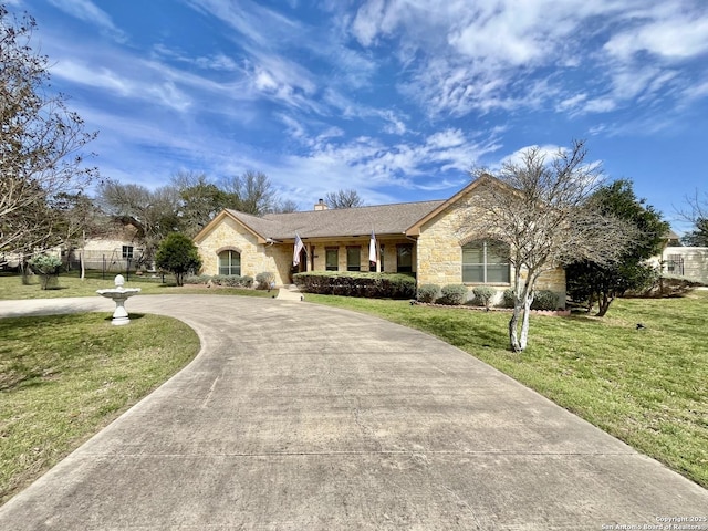 view of front of property featuring stone siding, a chimney, curved driveway, and a front lawn