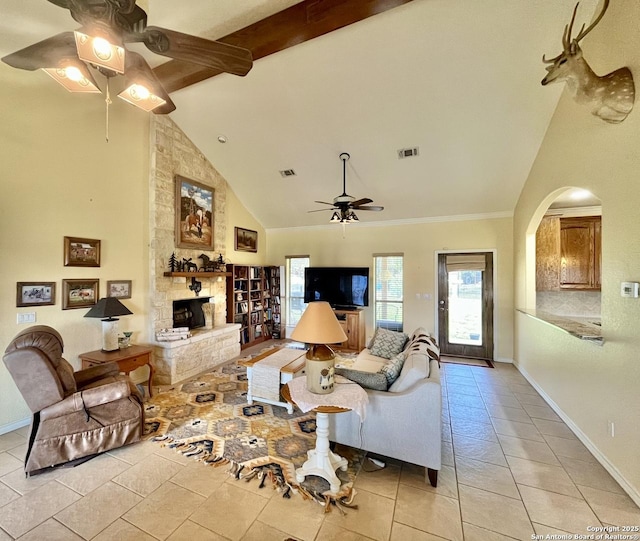 living room with visible vents, a ceiling fan, a stone fireplace, beamed ceiling, and baseboards