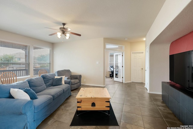 living area featuring a ceiling fan, dark tile patterned floors, and baseboards