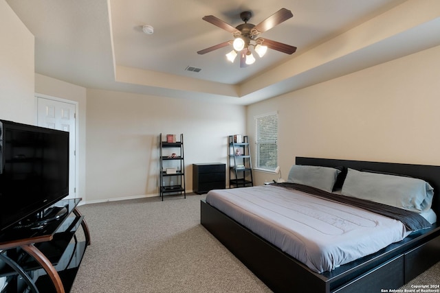 carpeted bedroom with ceiling fan, a tray ceiling, visible vents, and baseboards