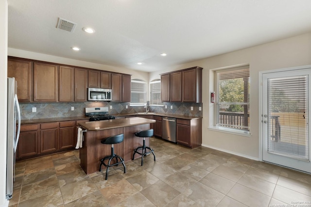 kitchen featuring tasteful backsplash, visible vents, a breakfast bar, a center island, and stainless steel appliances