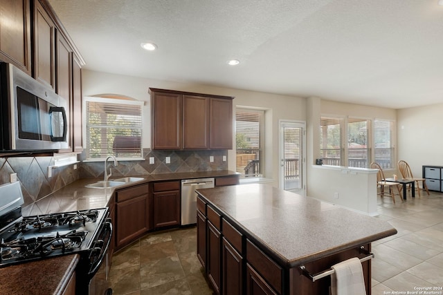 kitchen with dark countertops, backsplash, stainless steel appliances, and a sink