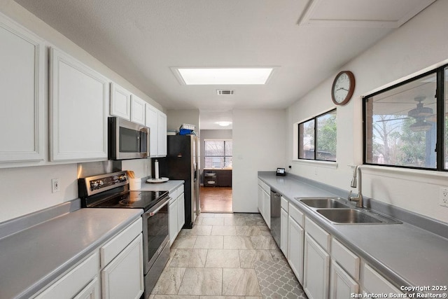 kitchen with stainless steel appliances, a sink, visible vents, white cabinets, and light countertops