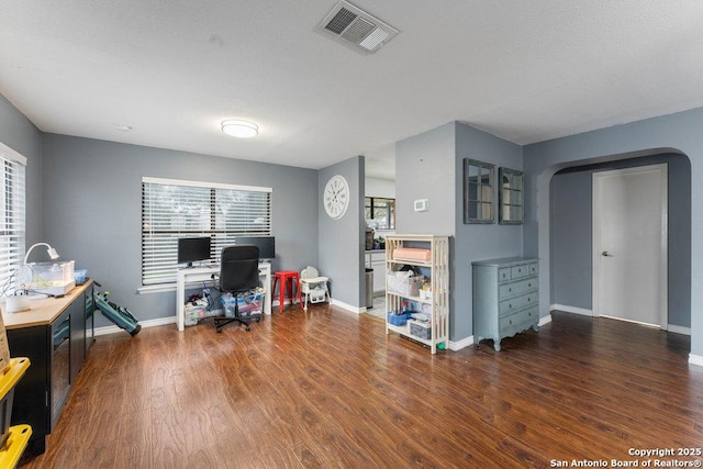 office area with arched walkways, visible vents, baseboards, and wood finished floors