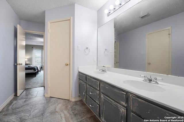 ensuite bathroom featuring a sink, a textured ceiling, baseboards, and double vanity