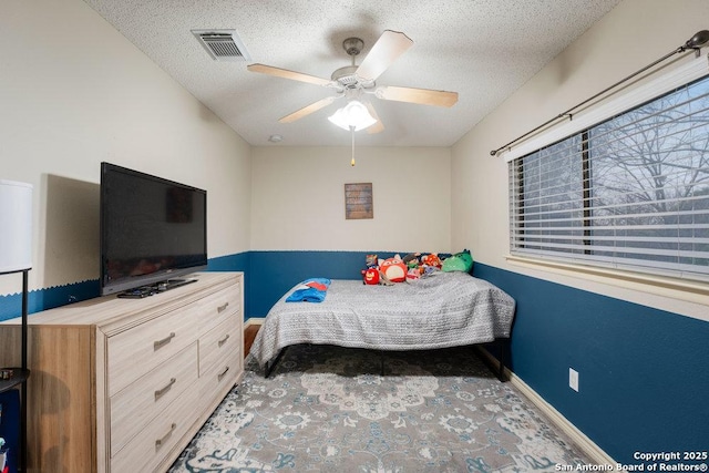 bedroom with a textured ceiling, a ceiling fan, visible vents, and baseboards