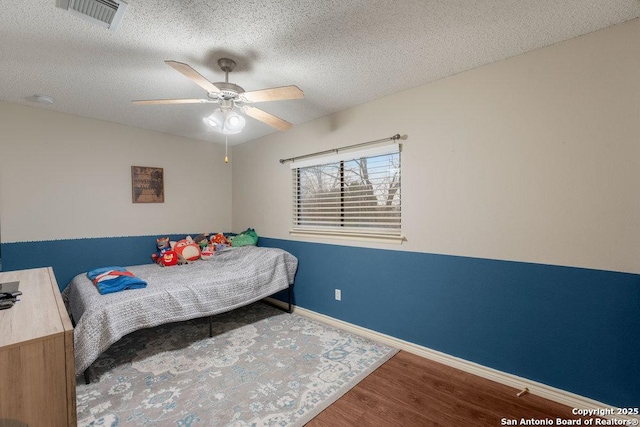 bedroom with visible vents, ceiling fan, a textured ceiling, wood finished floors, and baseboards