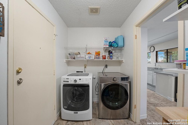 washroom featuring laundry area, independent washer and dryer, a textured ceiling, light wood-type flooring, and a sink