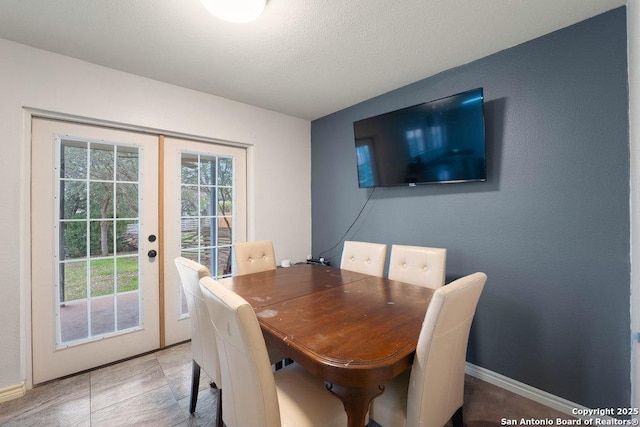 dining area with french doors, a textured ceiling, and baseboards