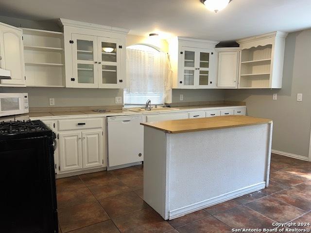 kitchen with white appliances, a sink, light countertops, open shelves, and glass insert cabinets