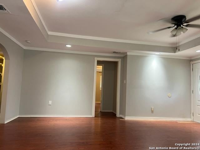 empty room with arched walkways, wood finished floors, baseboards, a tray ceiling, and crown molding