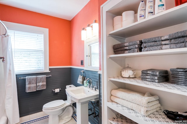 bathroom with toilet, plenty of natural light, tile walls, and wainscoting