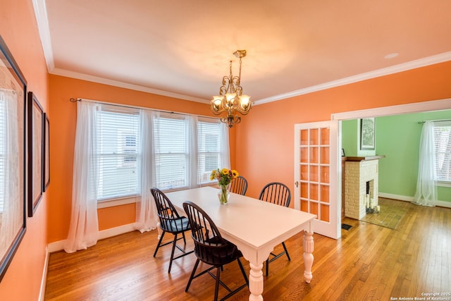 dining area featuring baseboards, ornamental molding, light wood-style floors, a fireplace, and a notable chandelier