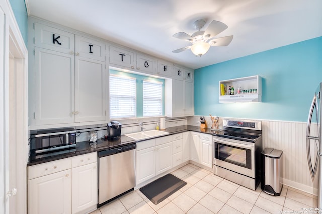 kitchen featuring wainscoting, dark countertops, appliances with stainless steel finishes, range hood, and a sink