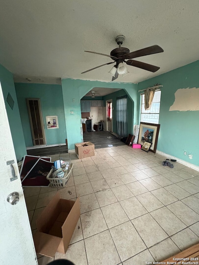 living area with arched walkways, ceiling fan, a textured ceiling, and light tile patterned floors