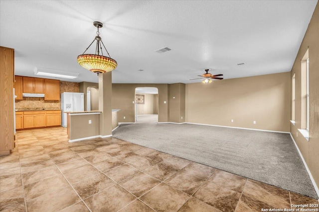 unfurnished living room featuring visible vents, arched walkways, baseboards, light colored carpet, and ceiling fan