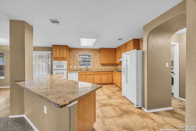 kitchen featuring arched walkways, visible vents, light stone countertops, white appliances, and a peninsula