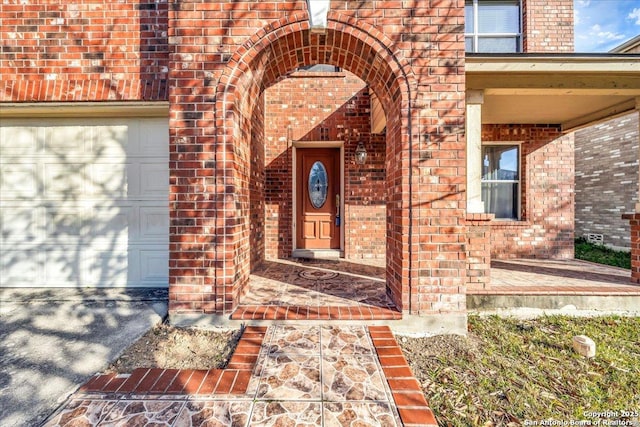 doorway to property featuring an attached garage, a porch, and brick siding