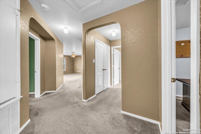 corridor with visible vents, arched walkways, a textured wall, carpet, and a textured ceiling