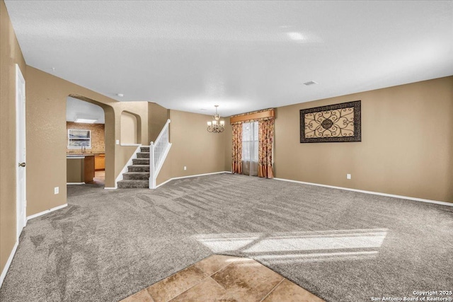 carpeted spare room with arched walkways, stairway, baseboards, and an inviting chandelier