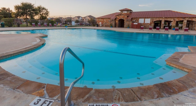 pool at dusk with a patio area, fence, and a community pool