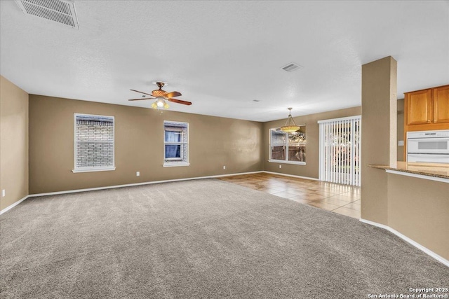 unfurnished living room featuring a ceiling fan, light carpet, visible vents, and a textured ceiling