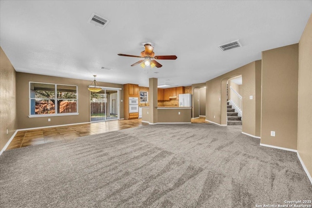 unfurnished living room featuring light carpet, stairway, ceiling fan, and visible vents