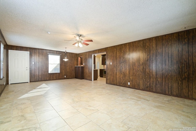 unfurnished living room with ceiling fan, a textured ceiling, and wooden walls