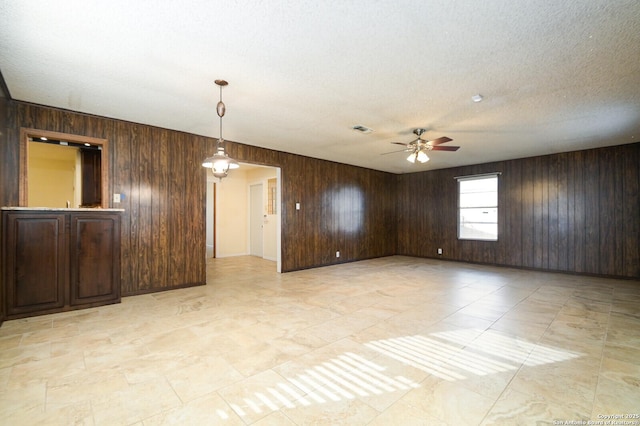 spare room with wood walls, visible vents, ceiling fan, and a textured ceiling