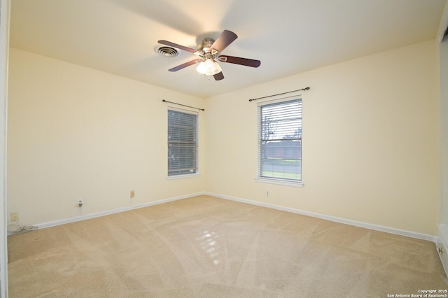 empty room featuring a ceiling fan, light colored carpet, visible vents, and baseboards