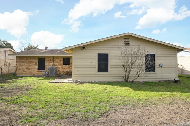 rear view of house featuring cooling unit, brick siding, a lawn, and fence