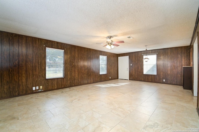 unfurnished room with wood walls, ceiling fan, visible vents, and a textured ceiling