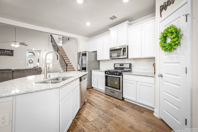 kitchen with arched walkways, decorative backsplash, appliances with stainless steel finishes, wood finish floors, and a sink