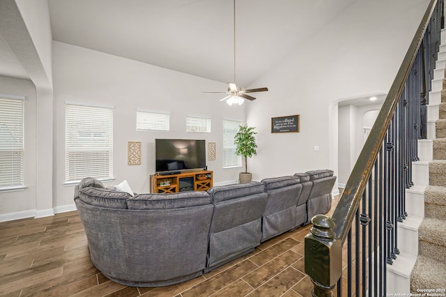 living area with baseboards, arched walkways, stairway, wood finish floors, and high vaulted ceiling