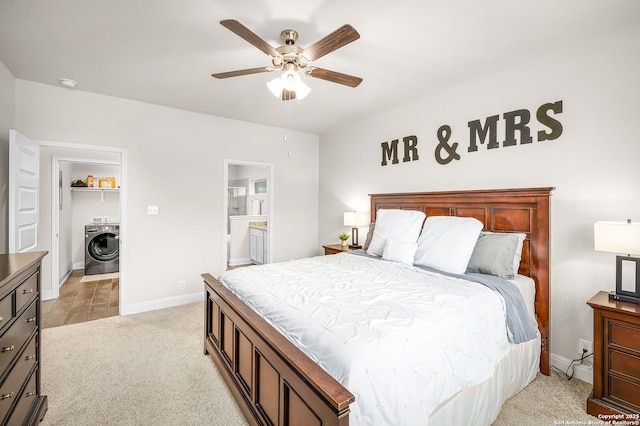 bedroom featuring ceiling fan, light carpet, baseboards, ensuite bath, and washer / dryer