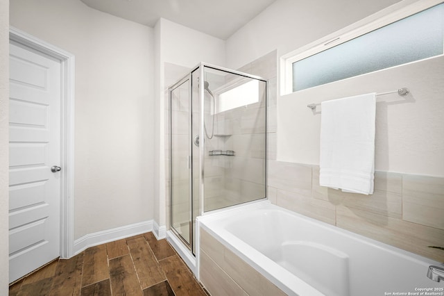 bathroom featuring a stall shower, baseboards, a bath, and wood finished floors