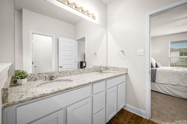 ensuite bathroom with double vanity, ensuite bath, a sink, and baseboards