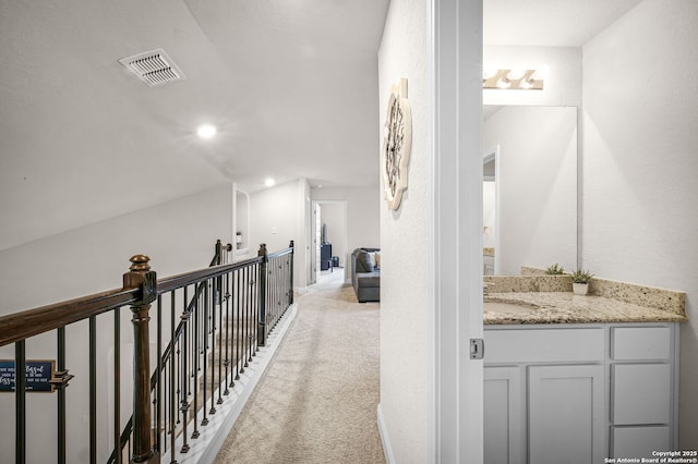 hall featuring light colored carpet, visible vents, vaulted ceiling, a sink, and an upstairs landing