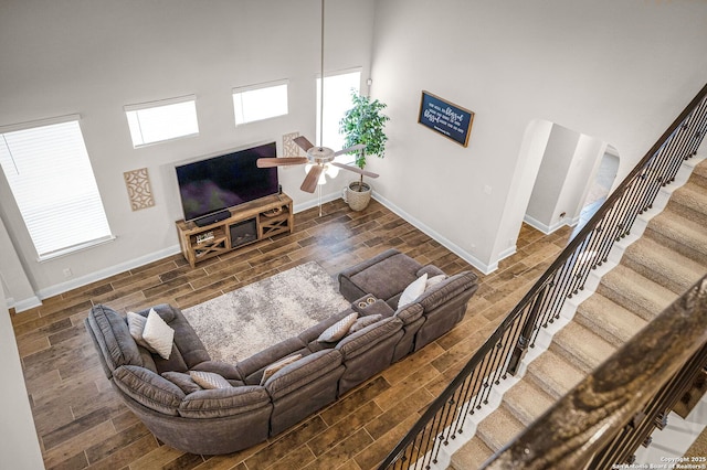 living area with a towering ceiling, baseboards, stairway, and wood finished floors