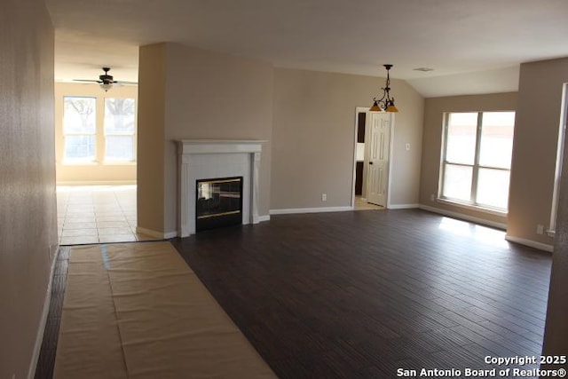 unfurnished living room with a healthy amount of sunlight, vaulted ceiling, a tiled fireplace, and wood finished floors