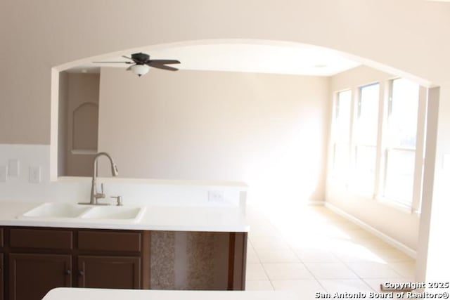 kitchen with arched walkways, light countertops, a ceiling fan, a sink, and dark brown cabinets