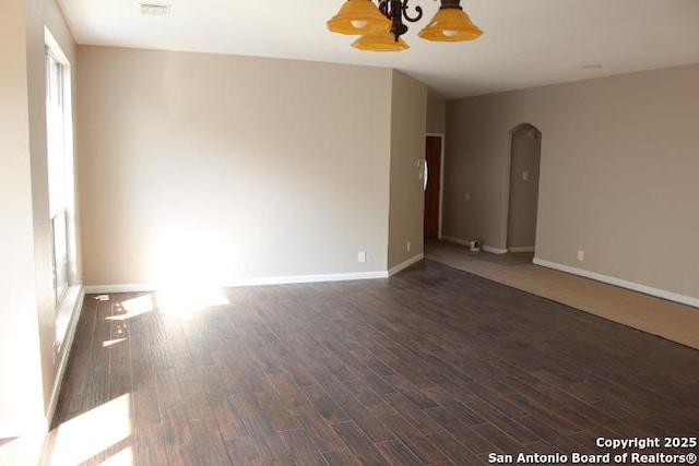 empty room with dark wood-style floors, arched walkways, and baseboards