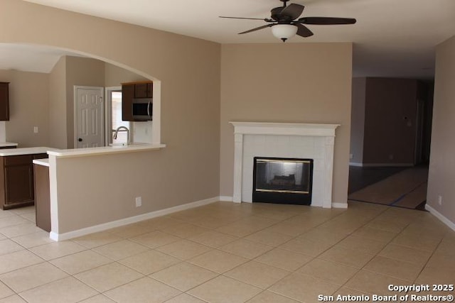 unfurnished living room with baseboards, a ceiling fan, a fireplace, a sink, and light tile patterned flooring