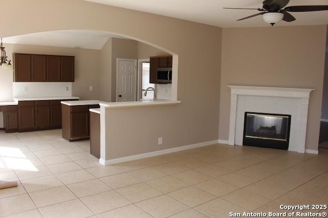 kitchen with a tile fireplace, ceiling fan, stainless steel microwave, light countertops, and light tile patterned flooring