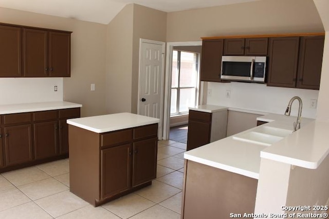 kitchen with light tile patterned floors, stainless steel microwave, a center island, light countertops, and a sink