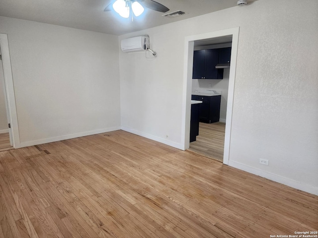 empty room featuring light wood finished floors, visible vents, baseboards, ceiling fan, and a wall mounted air conditioner