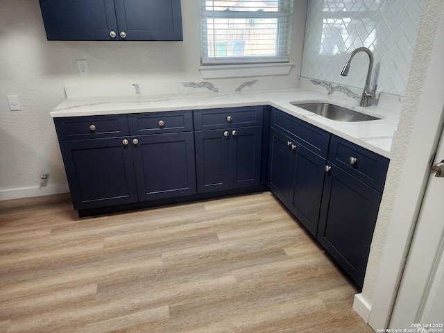 kitchen featuring blue cabinets, a sink, light wood-style flooring, and decorative backsplash