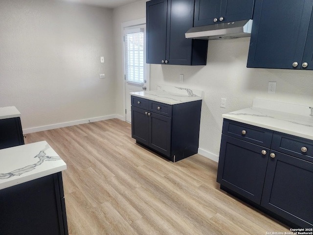 kitchen with light wood-type flooring, under cabinet range hood, baseboards, and light stone counters