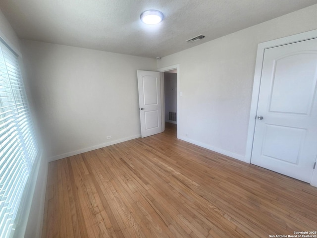 empty room featuring light wood-style floors, baseboards, visible vents, and a textured ceiling