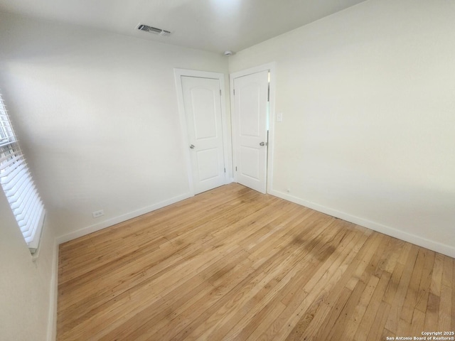 unfurnished room featuring light wood finished floors, visible vents, and baseboards